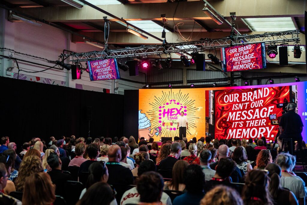 Marketing keynote presentation at MAD Fest London featuring big screens displaying a brand governance quote about creative performance and memory.
